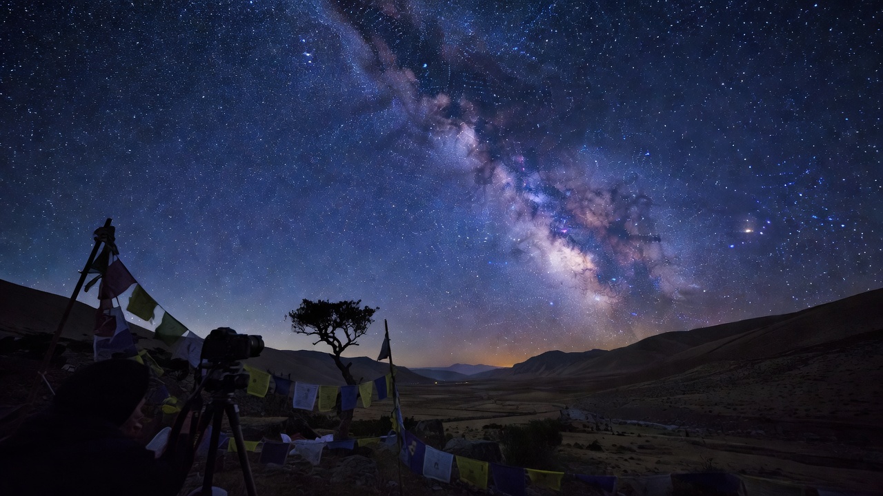 川西高原夜空下的银河与经幡前景，三脚架上的相机正在长时间曝光